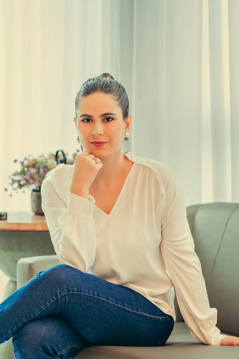 Dra. Laila Hassan sentada em um sofá junto à janela.